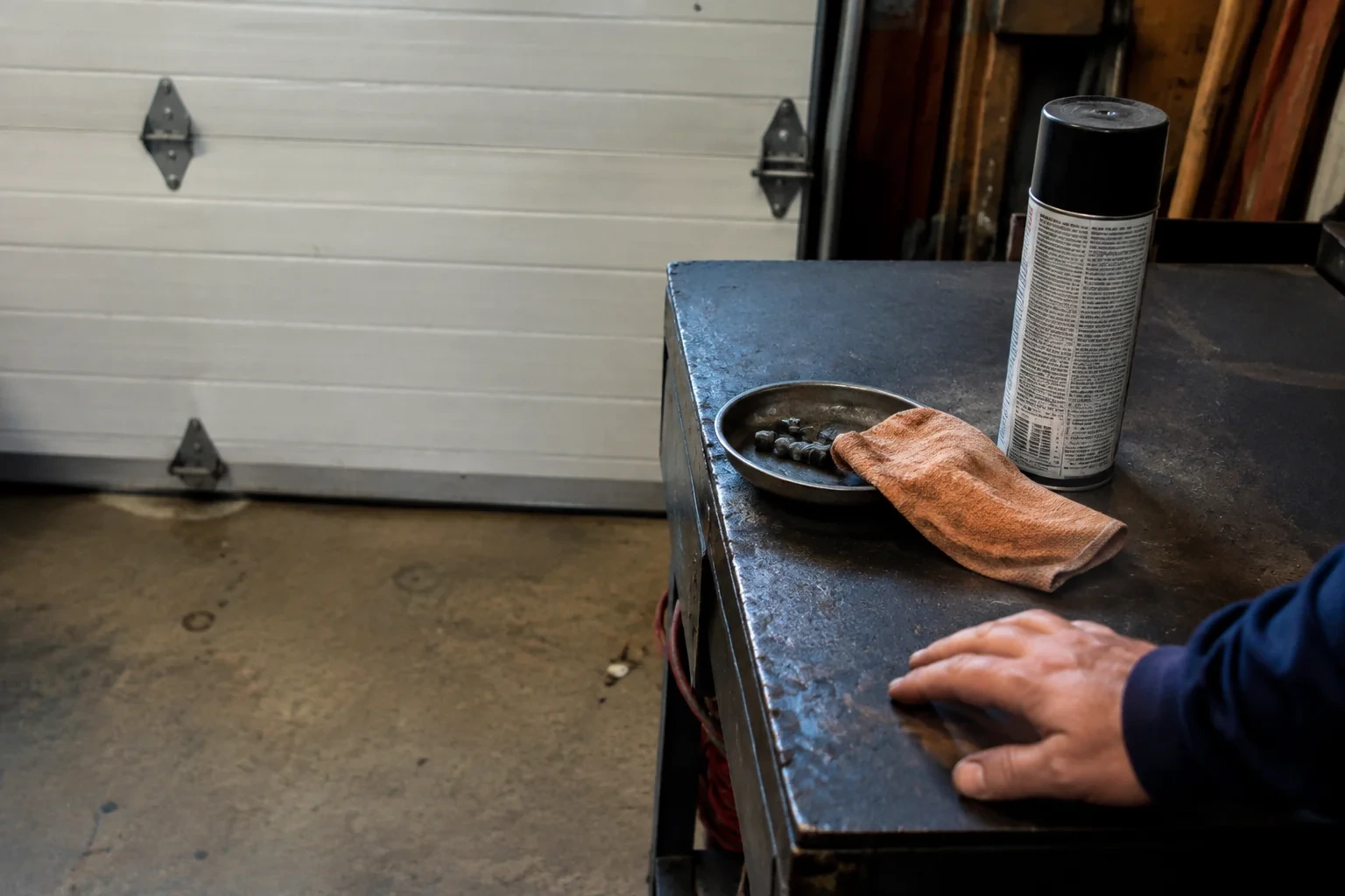 Capped service can, bolts and folded rag beside a hand on a garage workbench.
